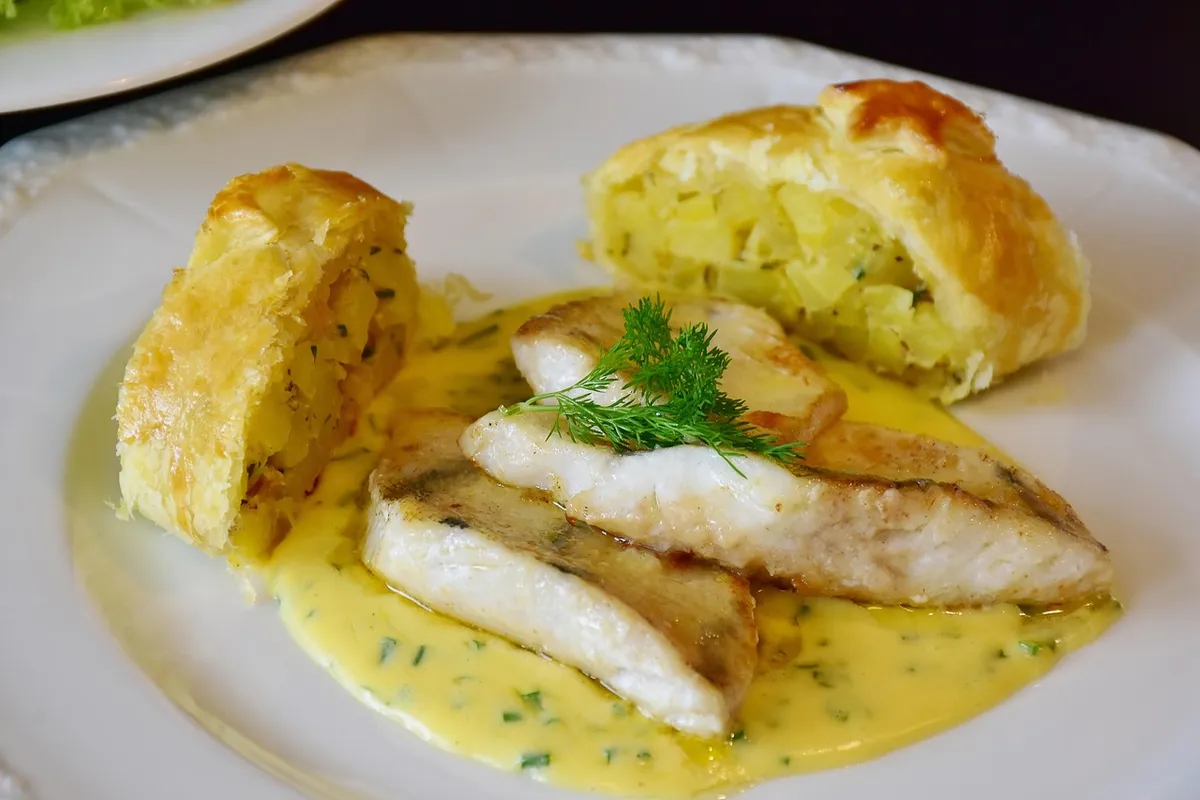 Lomos de merluza en salsa verde con patatas en un plato blanco