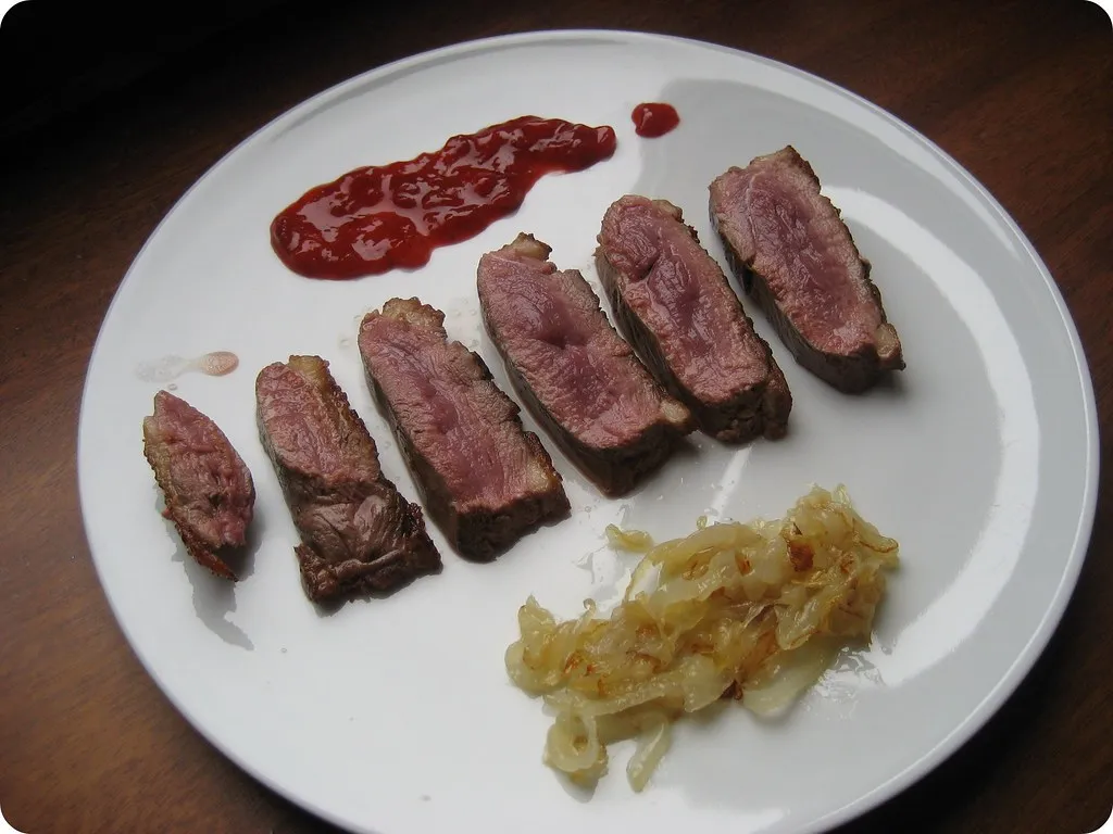 Pechuga de pato laminada junto a cebolla caramelizada, en un plato blanco